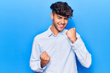 Gündelik giysiler giyen genç İspanyol adam şaşkınlık ve şaşkınlık içinde kollarını kaldırarak ve gözlerini kapayarak başarıyı kutluyor. 