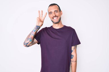 Dövmeli genç ve yakışıklı bir adam. Günlük giysiler giyiyor. Üç numaralı parmaklarıyla gösteriyor ve işaret ediyor.. 