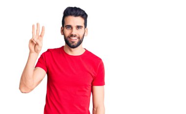 Sakallı, sıradan tişörtlü, üç numaralı parmaklarıyla gösteriş yapan, kendinden emin ve mutlu gülümseyen genç yakışıklı bir adam.. 