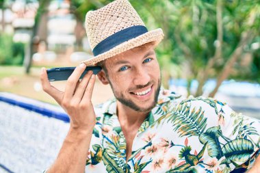 Beyaz tenli yakışıklı adam dışarıda mutlu bir şekilde gülümsüyor. Telefondaki sesli mesajı dinliyor.