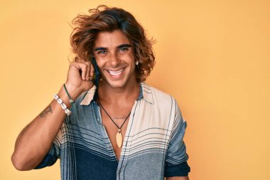 Genç İspanyol adam akıllı telefondan konuşuyor. Olumlu ve mutlu görünüyor. Kendine güvenen bir gülümsemeyle dişlerini gösteriyor. 