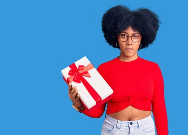 Genç Afro-Amerikan kızı elinde hediye tutarken şüpheci ve gergin, sorun yüzünden surat asıyor. negatif kişi. 