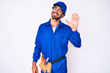 Kıvırcık saçlı ve ayı gibi giyinen yakışıklı genç adam merhaba diyor mutlu ve gülümsüyor, dostça karşılama jesti 