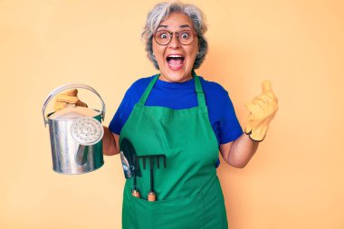 Bahçıvan önlüğü ve eldiven giyen yaşlı, beyaz saçlı kadın elinde su bidonu tutuyordu. Gururla bağırıyor, zaferi kutluyor ve başarıyı kollarını kaldırarak kutluyordu. 