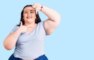 Gündelik kıyafetler giyen, gülümseyen, elleri ve parmakları mutlu yüzlü, çerçeveli genç bir kadın. yaratıcılık ve fotoğrafçılık kavramı. 