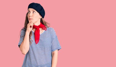 Fransız beresi ve çizgili tişört giyen genç ve güzel sarışın bir kadın bir soru hakkında endişeli ve gergin bir şekilde düşünüyor. 