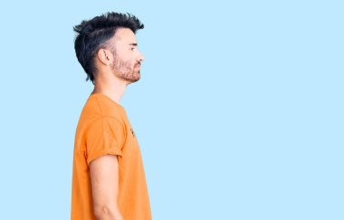 Üzerinde mutluluk mesajı olan İspanyol tişörtü giyen genç bir adam yan bakmak, rahat profil pozu vermek ve kendine güvenen bir gülümseme takınıyor.. 