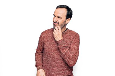 Orta yaşlı yakışıklı bir adam, günlük süveter giyer, izole edilmiş beyaz arka plan üzerinde durur, şüphe üzerine yoğunlaşır, çenesi parmaklarıyla yukarı bakar ve merak eder.