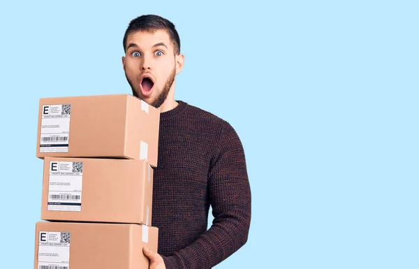 Young Handsome Man Holding Delivery Package Scared Amazed Open Mouth — Stock Photo, Image