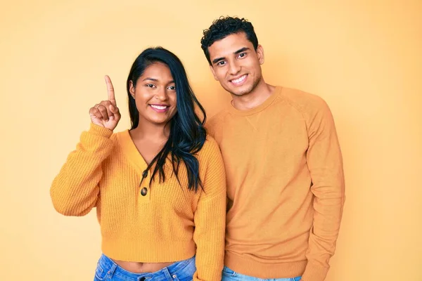 美しいラテン若いカップルを身に着けているカジュアル服一緒に示すと指の番号1を指摘しながら 自信と幸せ笑みを浮かべて — ストック写真