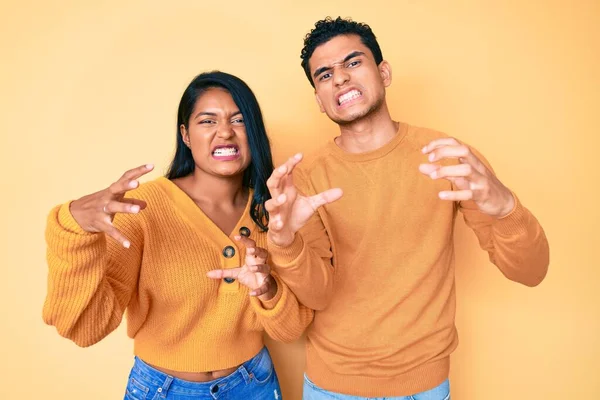 Beautiful latin young couple wearing casual clothes together shouting frustrated with rage, hands trying to strangle, yelling mad
