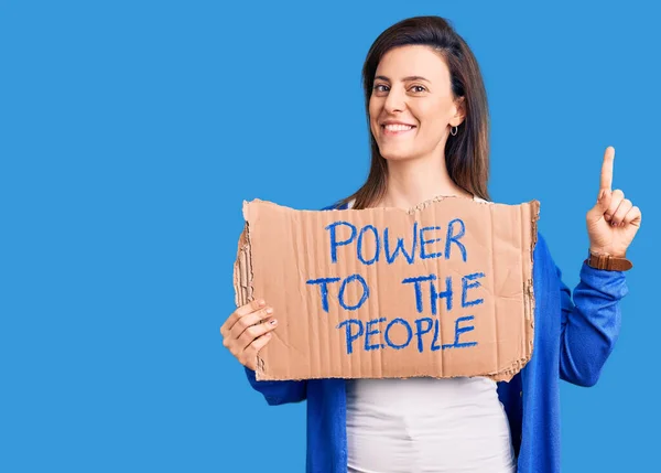 Young beautiful woman holding power to the people banner surprised with an idea or question pointing finger with happy face, number one