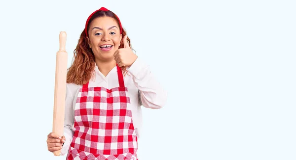 Jovem Latina Vestindo Avental Segurando Amassadeira Sorrindo Feliz Positivo Polegar — Fotografia de Stock