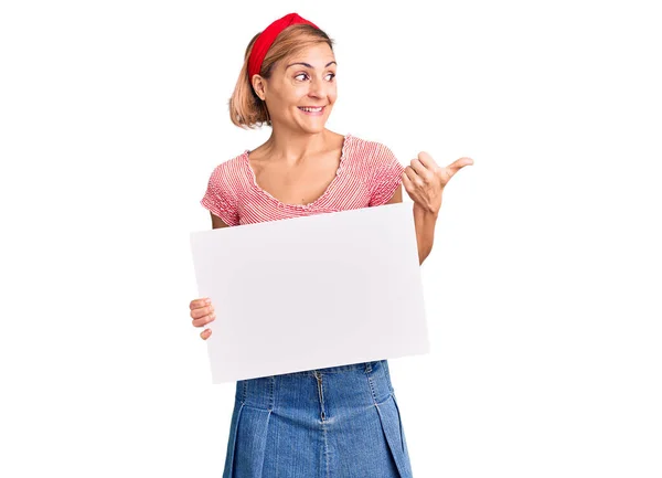 Mujer Rubia Joven Sosteniendo Banner Vacío Blanco Apuntando Con Pulgar —  Fotos de Stock