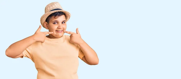 夏の帽子とハワイの水着を身に着けている小さな男の子は 明るい表情と指の歯と口で指して笑っています 歯の健康の概念 — ストック写真