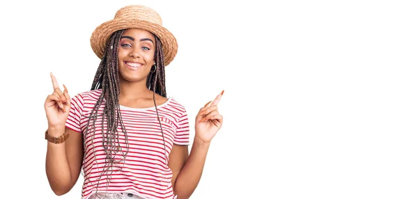 头戴夏帽 头戴辫子的年轻的非洲裔美国女人带着自信的微笑 手指指向不同的方向 复制广告空间 — 图库照片