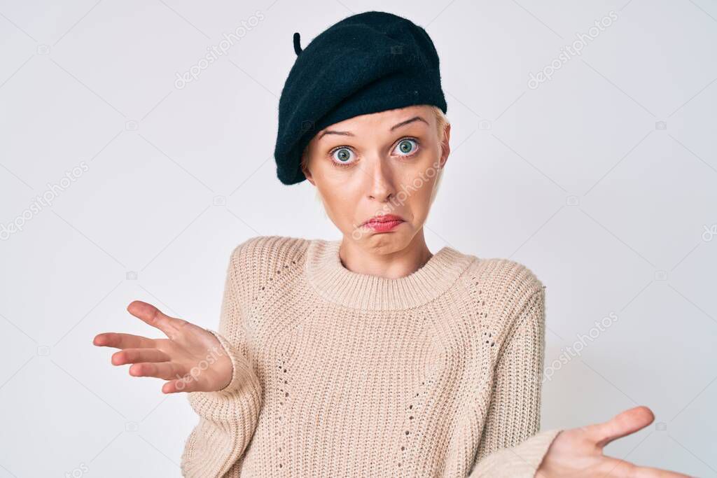 Young blonde woman wearing french look with beret clueless and confused expression with arms and hands raised. doubt concept. 