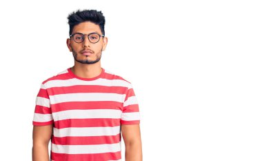 Yakışıklı Latin Amerikalı sıradan kıyafetler ve gözlük takan genç adam yüzünde ciddi bir ifadeyle rahatlamış. Basit ve doğal bir şekilde kameraya bakıyorsun.. 