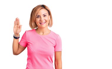 Spor kıyafeti giyen genç sarışın kadın merhaba diyor mutlu ve gülümsüyor, dostça karşılama hareketi yapıyor. 