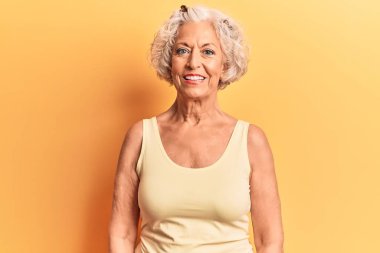 Yaşlı, gri saçlı, sıradan kıyafetler giyen, yüzünde mutlu ve havalı bir gülümseme olan bir kadın. şanslı kişi. 