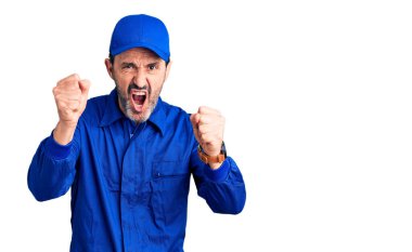 Orta yaşlı yakışıklı tamirci üniforması giyen kızgın ve kızgın yumruk kaldıran öfkeli bir adam öfkeyle bağırıyor. öfke ve agresif konsept. 