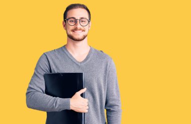 İş dosyasını tutan yakışıklı beyaz bir adam. Pozitif ve mutlu görünüyor. Kendine güvenen bir gülümsemeyle dişlerini gösteriyor. 