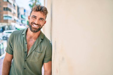 Genç İspanyol adam gülümsüyor. Mutlu bir şekilde şehrin duvarına yaslanıyor.