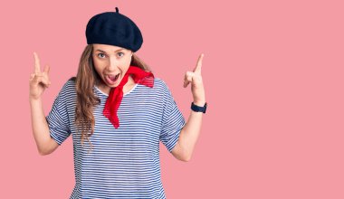 Fransız beresi takan, çizgili tişört giyen, çılgın bir ifadeyle bağıran, elleri havada rock sembolü yapan genç, güzel sarışın bir kadın. Müzik yıldızı. ağır müzik konsepti. 