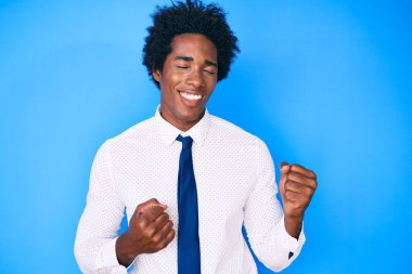 Afro saçlı, iş gömleği ve kravatlı yakışıklı Afro-Amerikalı adam. Kolları havada ve gözleri kapalı bir şekilde başarıyı kutluyor ve şaşırıyor. 