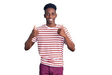 Genç afro-amerikan adam günlük kıyafetler giyiyor başarı işareti yapıyor, elleriyle olumlu jest yapıyor, gülümsüyor ve mutlu. Neşeli ifade ve kazanan jest. 