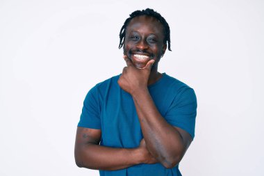 Saçları örgülü, kolları çapraz ve elleri çenesinde kameraya gülümseyen, kendinden emin genç Afro-Amerikan bir adam. Olumlu düşünmek. 