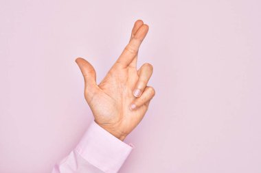 İzole edilmiş pembe arka plan üzerinde parmaklarını gösteren beyaz bir gencin eli. Parmakları çapraz, batıl inançlar ve şanslı bir jest, şanslı ve umut dolu bir ifade.