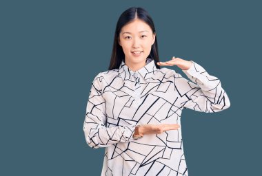 Genç, güzel, Çinli bir kadın, sıradan bir tişört giyiyor. Elleri büyük ve büyük bir işaret gösteriyor. Ölçü sembolü. Kameraya bakıp gülümsüyor. ölçüm kavramı. 