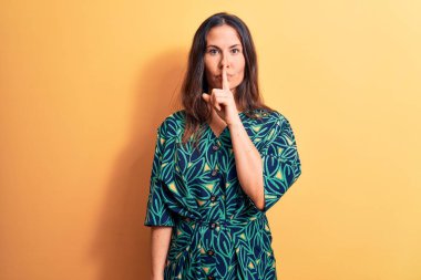 Sarı arka planda dikilmiş sıradan bir çiçekli elbise giyen genç ve güzel esmer kadın sessiz olmak istiyor. Sessizlik ve gizli konsept.