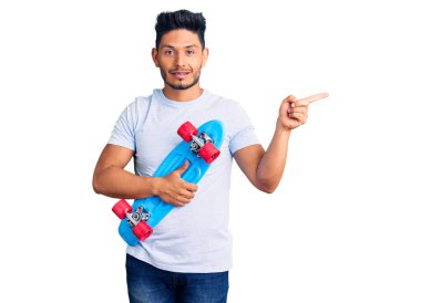 Yakışıklı Latin Amerikalı genç kaykaycı. Gülümsüyor. Elleri ve parmakları yana doğru uzanıyor. 