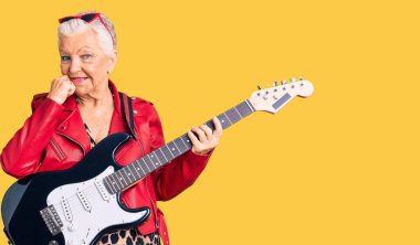 Son sınıf güzeli, mavi gözlü, gri saçlı modern görünümlü, eli çenesinde elektro gitar çalan soru soran, düşünceli bir kadın. Gülümseyen ve düşünceli bir yüz. şüphe kavramı. 