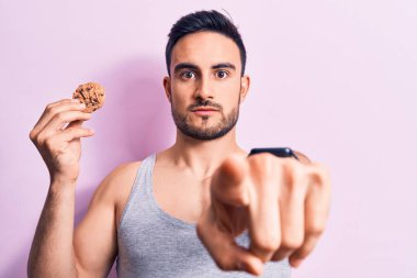 Sakallı, kolsuz tişörtlü, çikolatalı kurabiye yiyen, kamerayı işaret eden ve kendine güvenen genç, yakışıklı bir adam.