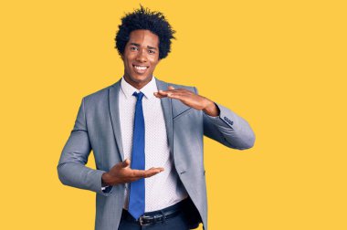 Afro saçlı, iş ceketi giyen, elleri büyük ve büyük boy işareti gösteren, ölçü sembolü olan yakışıklı Afro-Amerikan bir adam. Kameraya bakıp gülümsüyor. ölçüm kavramı. 