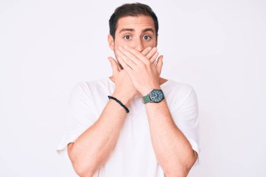 Gündelik beyaz tişört giyen genç yakışıklı adam yanlışlıkla elleriyle ağzını kapatırken şok oldu. gizli kavram. 