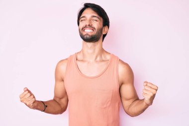 Yakışıklı İspanyol adam gündelik kıyafetler giyiyor. Çok mutlu ve heyecanlı. Kolları havada, gülümseyen ve başarı için bağıran kazanan bir jest yapıyor. kutlama konsepti. 