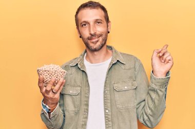 Genç yakışıklı adam elinde nohut kasesi tutarken mutlu bir şekilde gülümsüyor. 