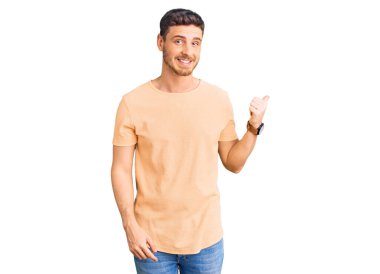 Ayılı yakışıklı, sıradan sarı tişörtlü, mutlu yüzlü, gülümseyen ve baş parmağıyla yan tarafı gösteren genç adam.. 