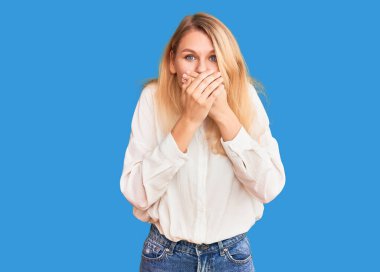 Gündelik tişört giyen genç ve güzel sarışın kadın yanlışlıkla elleri ile ağzını kapatırken şok oldu. gizli kavram. 