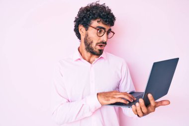 Kıvırcık saçlı ve ayı gibi çalışan yakışıklı bir genç bilgisayar bilgisayarı kullanıyor. Şaşırmak için ağzı açık ve korkmuş, inançsız bir yüz. 