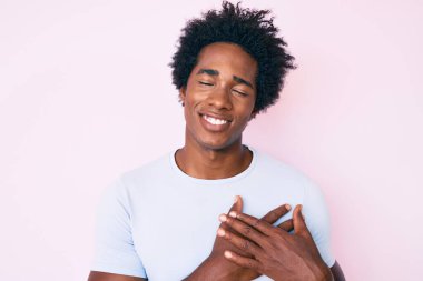 Yakışıklı Afro saçlı, sıradan kıyafetler giyen, göğsünde elleri kapalı, yüzünde minnet dolu bir jest olan Afro-Amerikan erkeği. sağlık kavramı. 