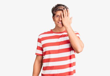 Gündelik kıyafetler giyen genç yakışıklı adam bir gözünü eliyle kapatıyor, yüzünde kendine güvenen bir gülümseme ve şaşırtıcı bir duygu var.. 