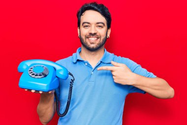 Antika telefon tutan genç İspanyol adam gülümseyerek el ve parmağıyla işaret ediyor. 