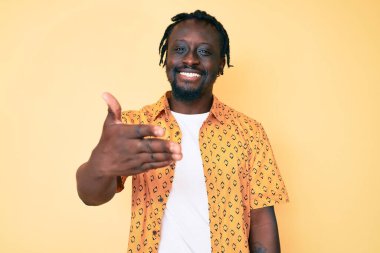 Örgülü, sıradan kıyafetler giyen, dostça gülümseyerek tokalaşan genç Afro-Amerikan erkeği selamlama ve hoş geldin demek için. başarılı iş. 