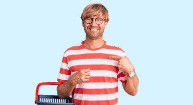 Sakallı, süpermarket alışveriş sepeti tutan yakışıklı beyaz adam gülümseyen ve gururlu birini işaret ediyor. 