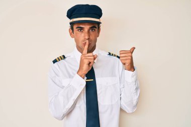 Uçak pilotu üniforması giyen genç İspanyol adam sessiz olmak istiyor. Parmakları dudaklarında, elleri yandan işaret ederek. sessizlik ve gizli konsept. 